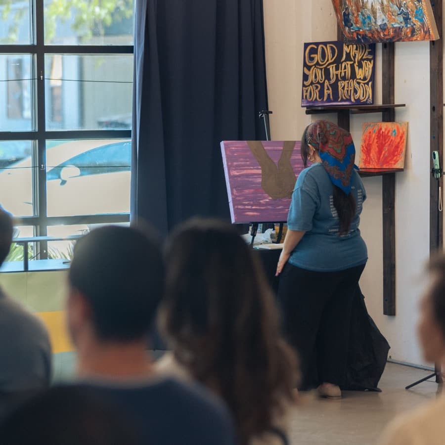 An artist paints live on stage while people watch.
