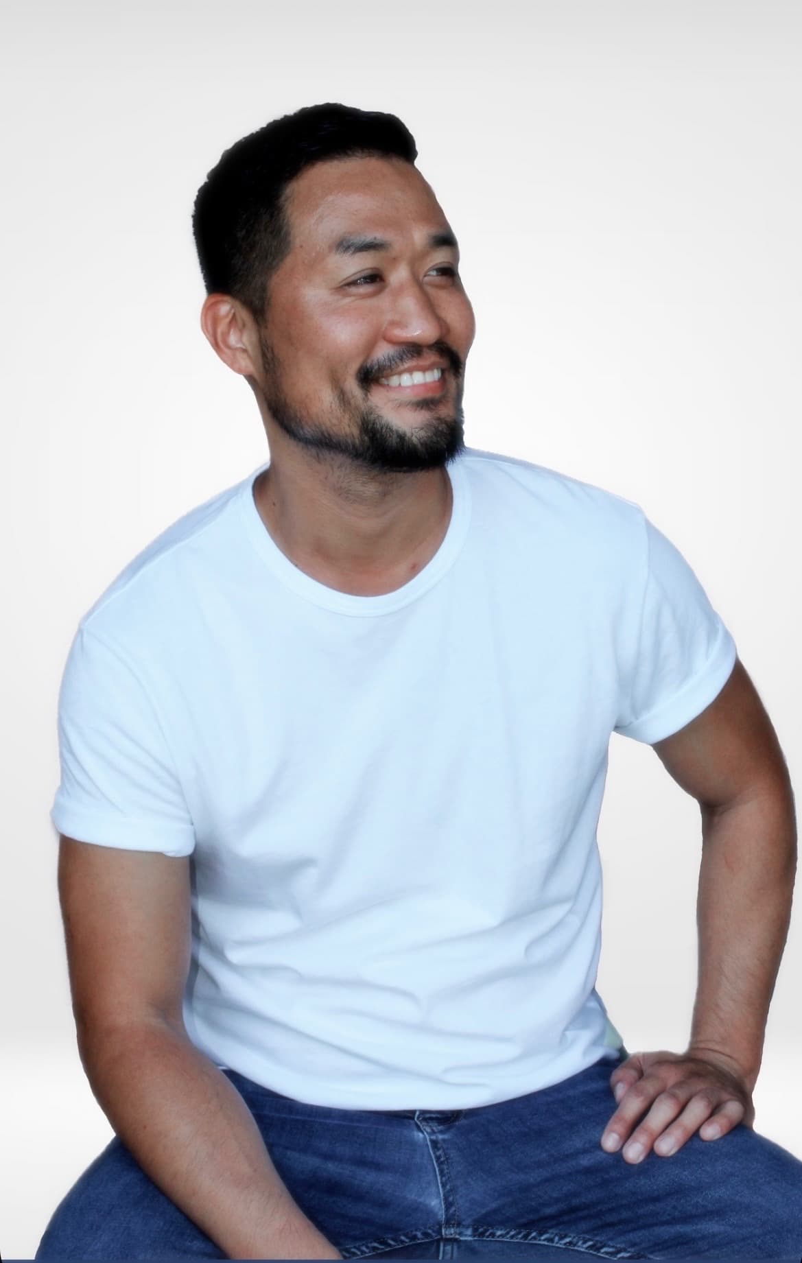 Pastor John Lee in a white T-shirt, seated and smiling, looking off to one side