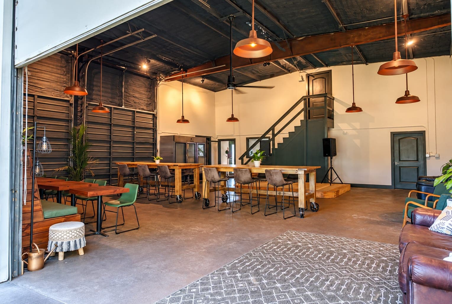 Inside Sapien Center: long wooden tables and stools on a concrete floor, copper pendant lights, and a small stage under a stair